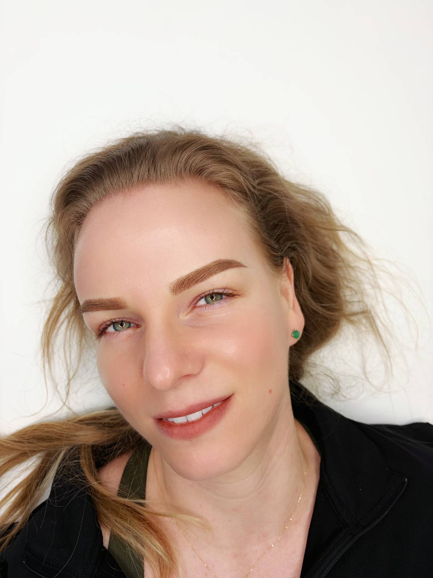A client with long light-brown hair, smiling, photographed at the end of the appointment with fresh auburn brows.