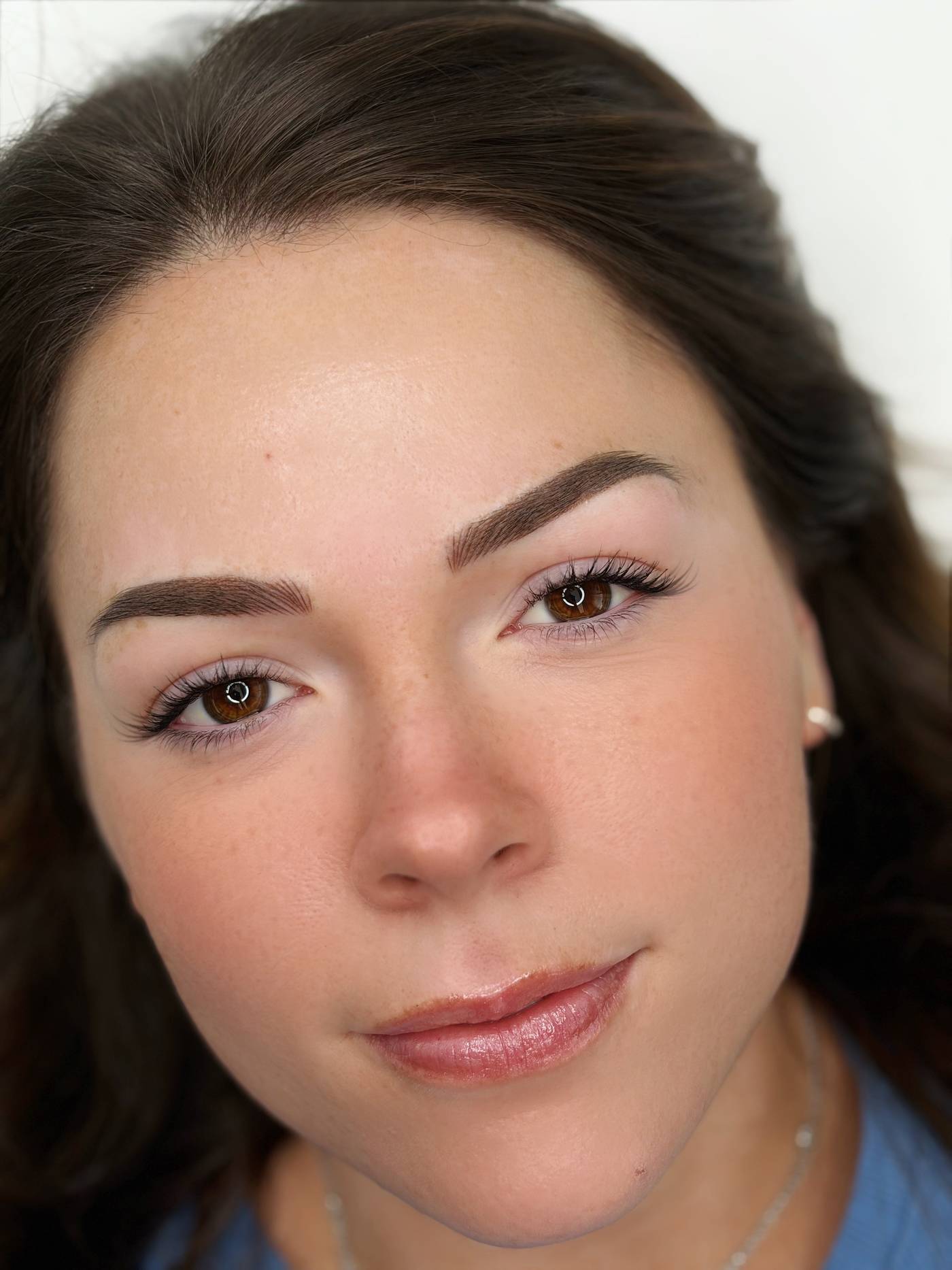 A client with dark hair and freckles, photographed close at the end of the appointment, with fresh brown brows.